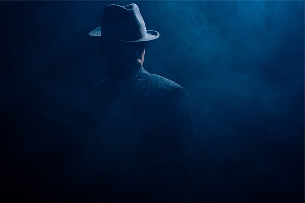 silhouette of mafioso in felt hat and suit on dark thumbnail